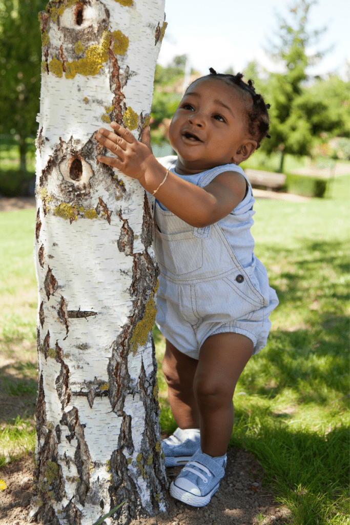 A baby explores the textures of tree bark during outdoor play.