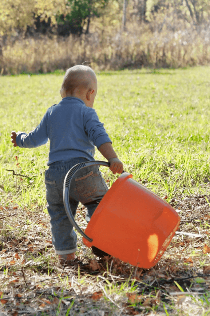 A baby walks outside dragging a bucket during a push and pull sensory activity.