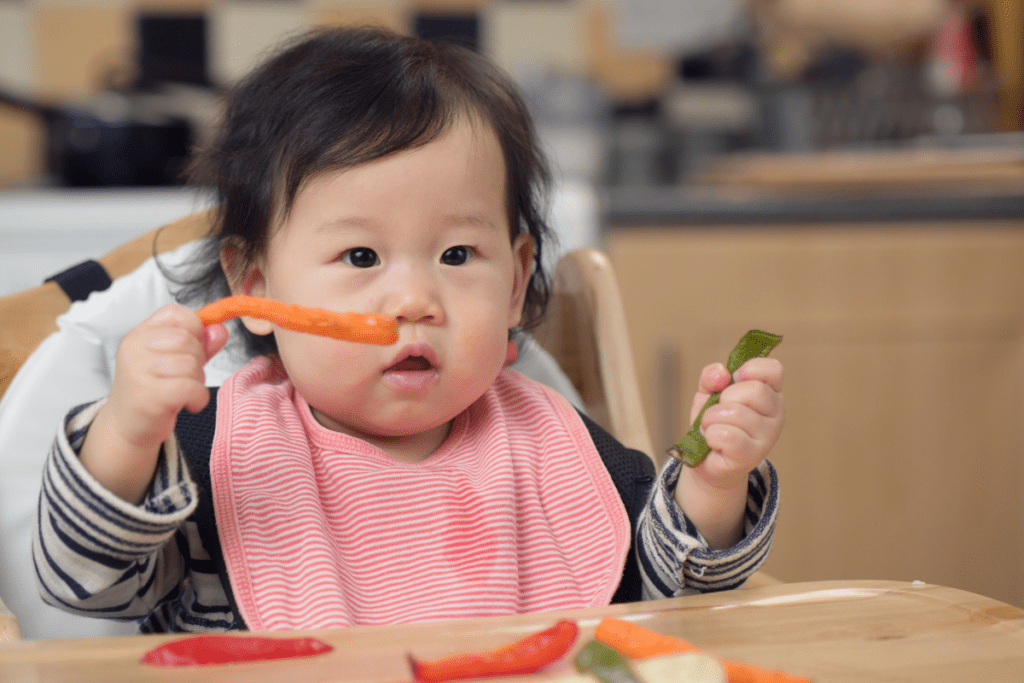 A baby touches and tastes sliced vegetables during a snack time sensory activity.