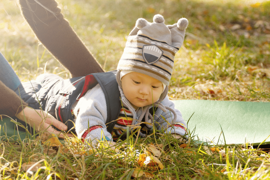A baby plays outside and explores how the grass feels during a tummy time sensory activity.