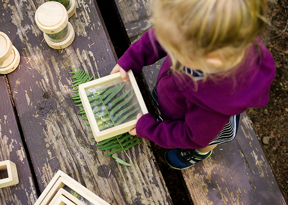Preschool girl observing nature's treasures using Guidecraft's Treasure Tubes and Clear Treasure Blocks 