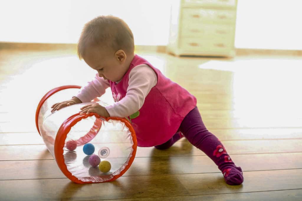 A baby pushes a rolling cylinder toy and explores the balls inside it.