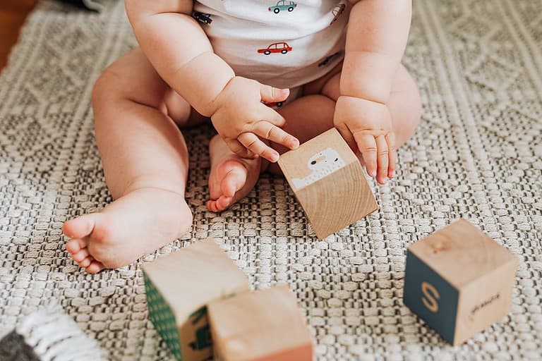 Baby plays with wooden blocks on the floor.