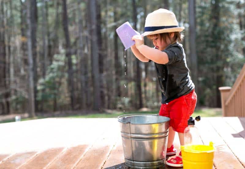 Happy toddler boy playing outside with buckets of water