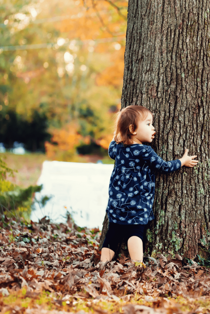 toddler hugs tree looking surprised