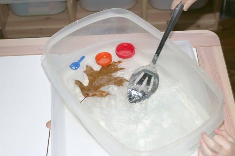 preschooler using metal spoon to stir water in sensory bin