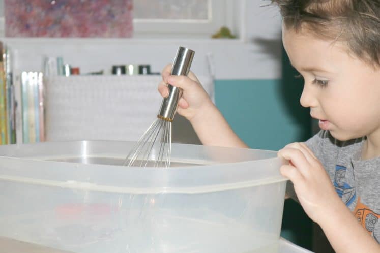 preschooler stirring water with metal whisk