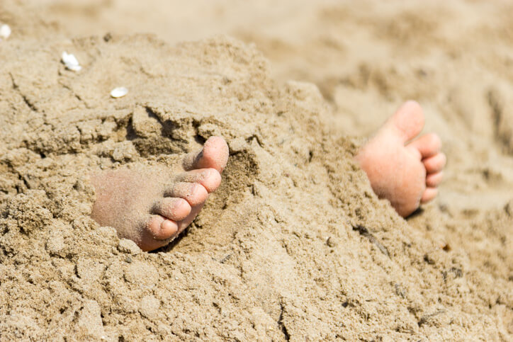 Human feet buried in sand.