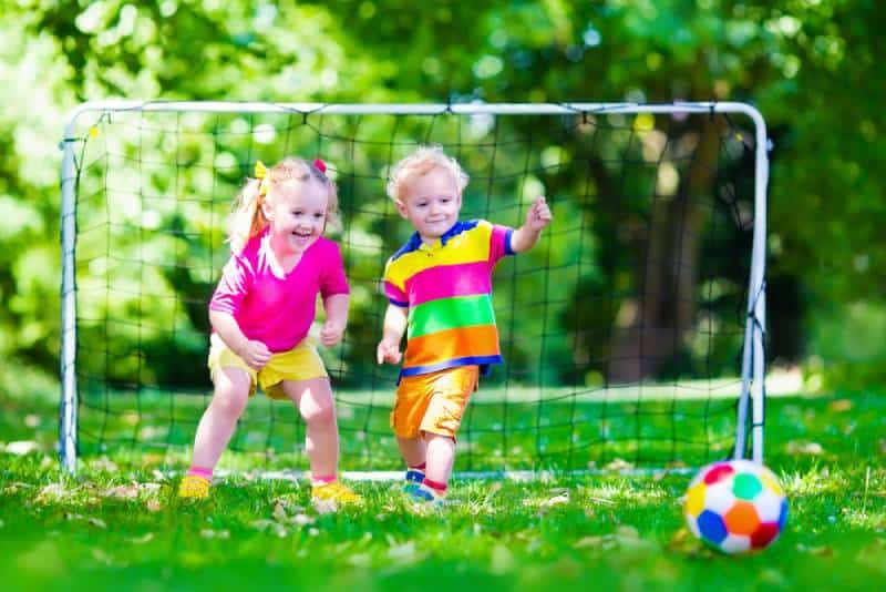 Two happy children playing football outdoors in school yard in summer