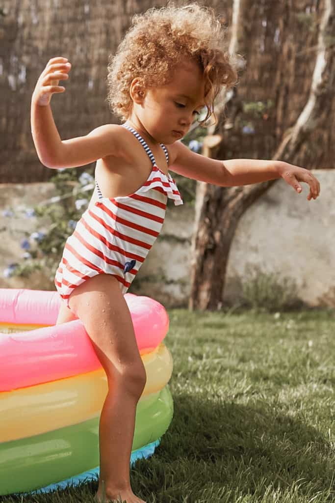 Girl in a swimsuit stepping out of a kiddie pool after doing a kiddie pool activity.