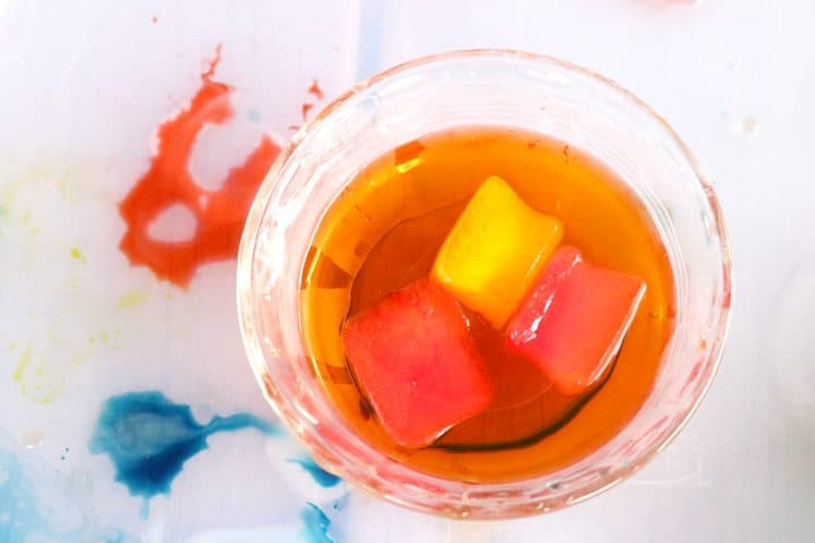 dish containing orange water with red and yellow ice cubes