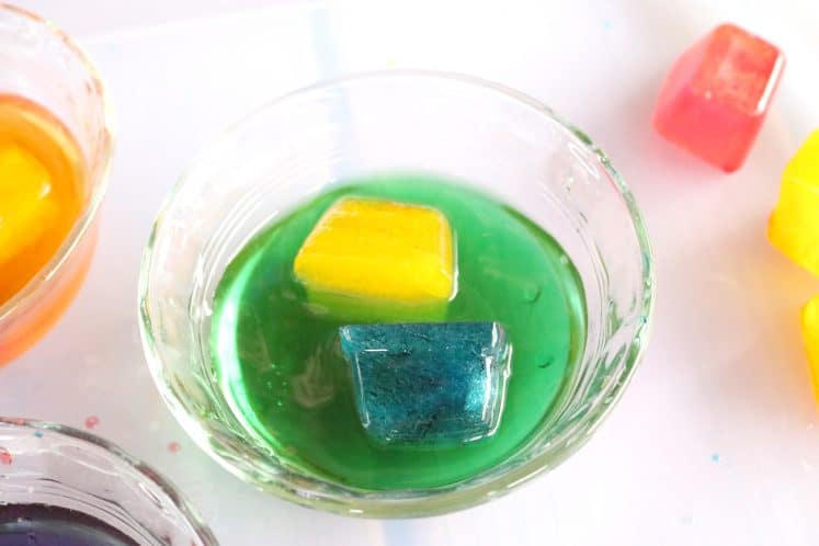 dish of green water containing yellow and blue ice cubes