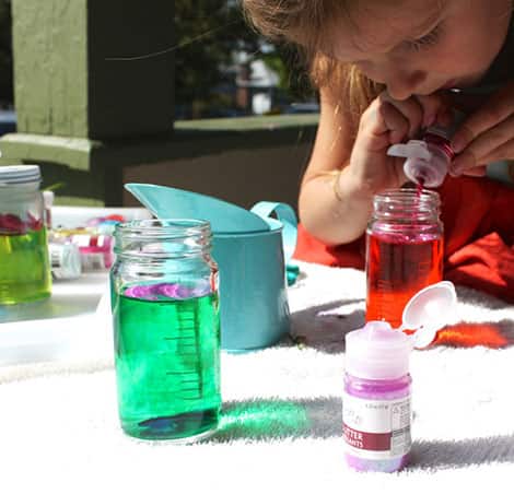 A young girl concentrates as she pours glitter into a jar of potion.