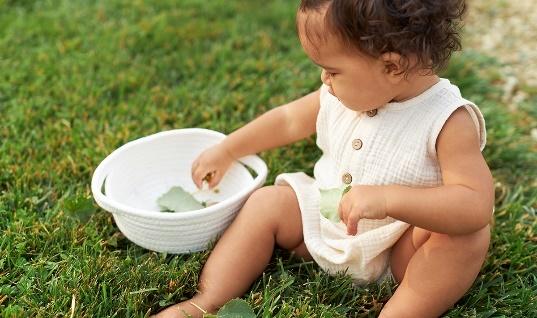 Baby sitting on the grass putting leaves in a basket
