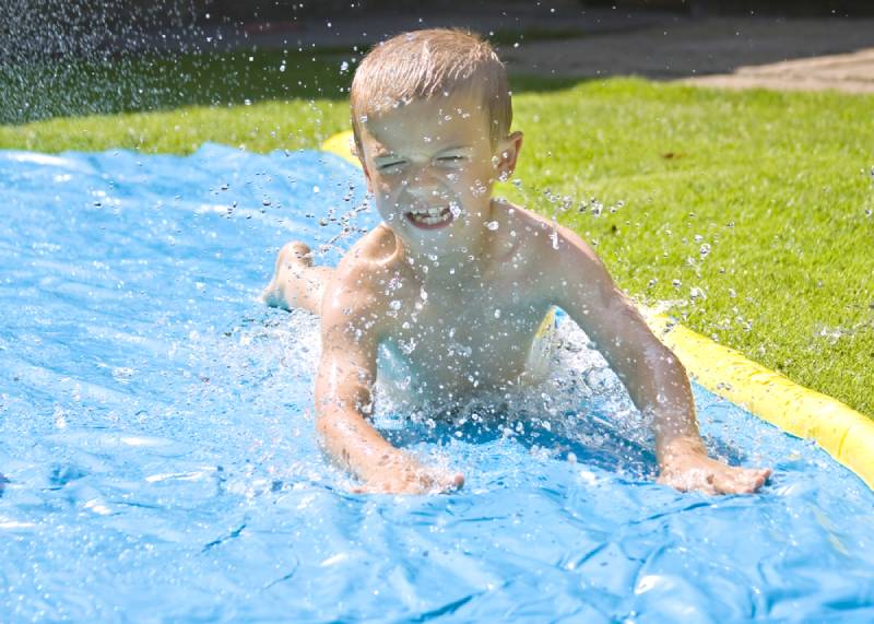Young boy sliding on a water slide in the back yard
