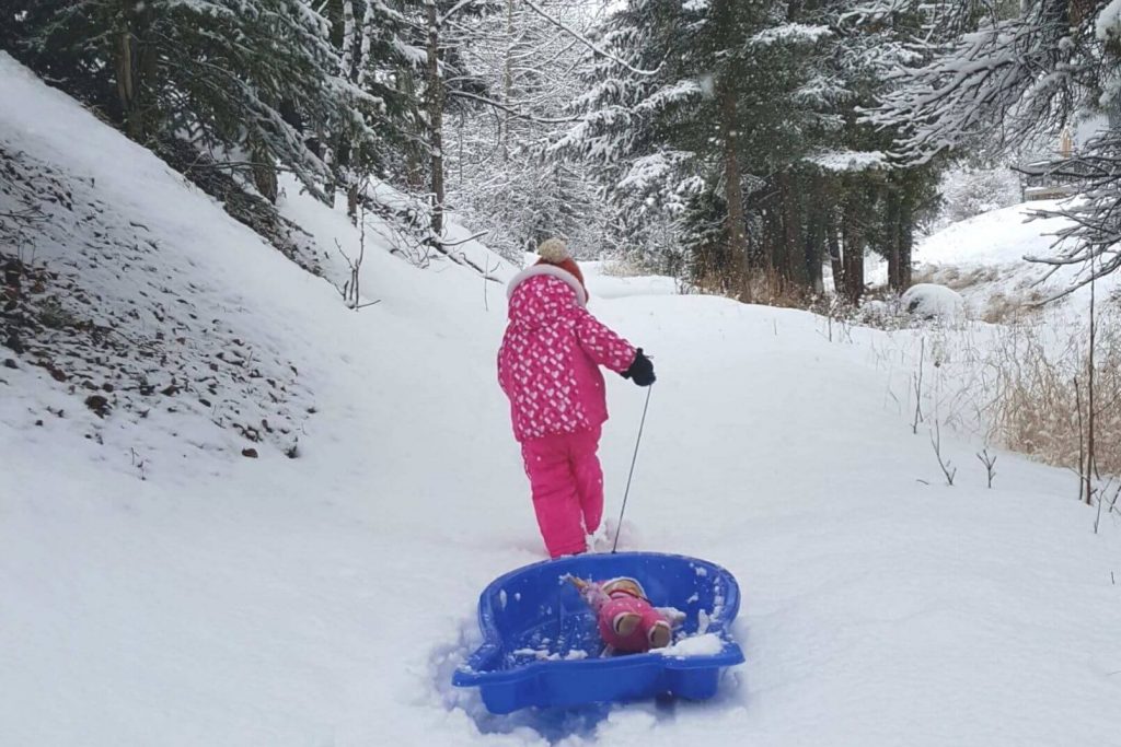 a little kid pulling her doll in a sled through the winter snow