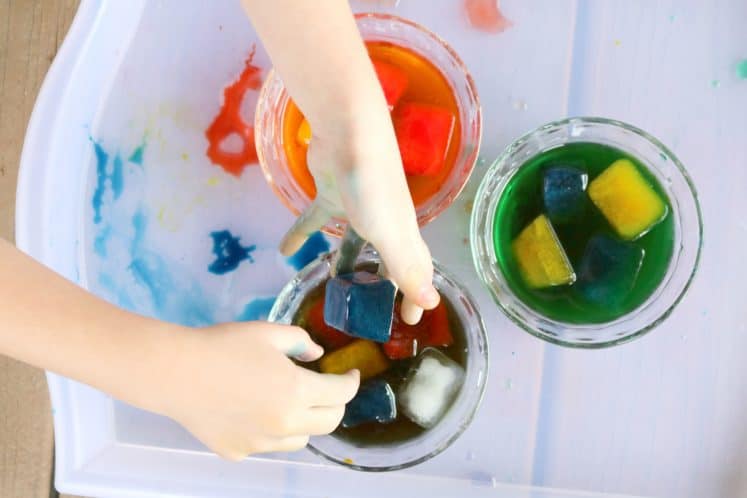 preschooler dropping colored ice cubes into dish of water