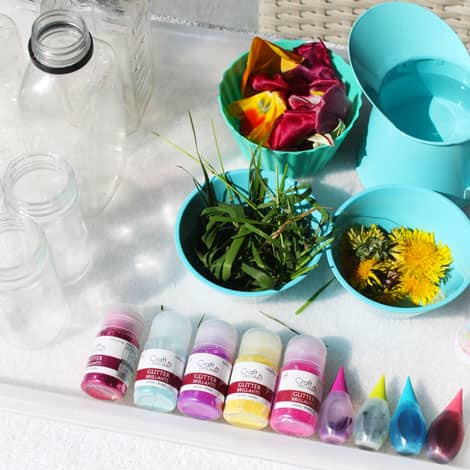 Glass bottles, bottles of glitter and bowls filled with petals, grasses and coloured water.