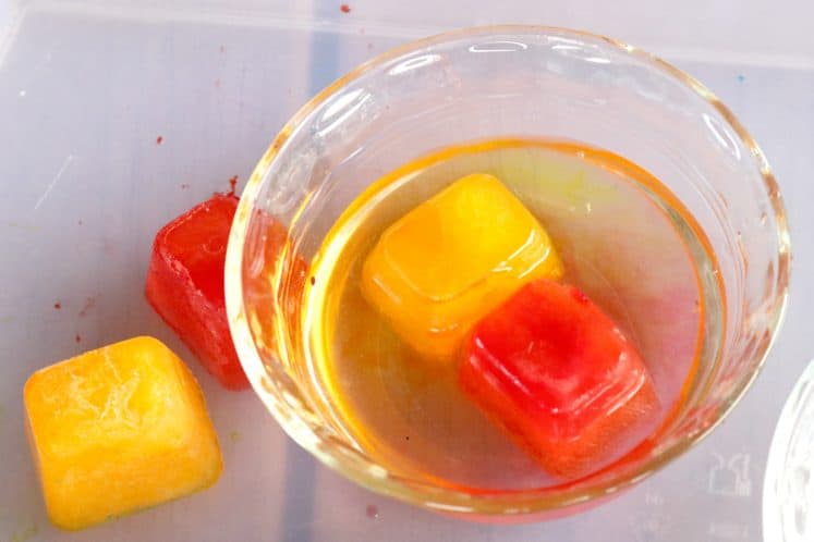 red and yellow colored ice cubes in clear dish filled with water