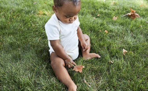 Baby sitting outside on the grass looking down at a leaf