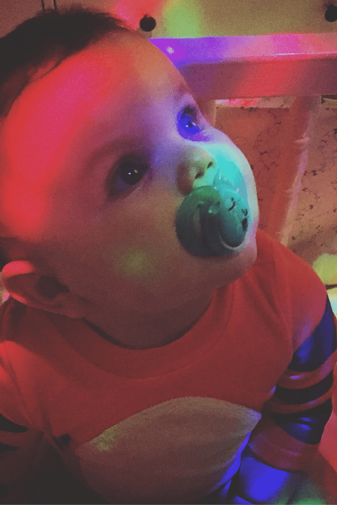 A baby looking up with red and green lights on their face during a sensory activity.