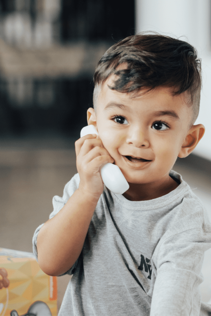 A toddler holding a toy phone to his ear and talking during a language activity.